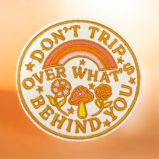 Embroidered patch with text 'Don't trip over what you behind' and a rainbow on a gradient background