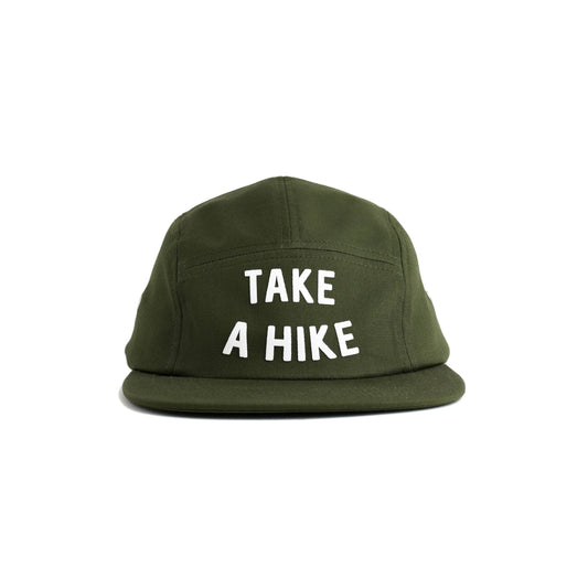 An olive green 5-panel cap with the phrase 'TAKE A HIKE' printed in bold white capital letters on the front, set against a plain white background. Green hat reads "take a hike" in turquoise flocked lettering on a seam free front panel.