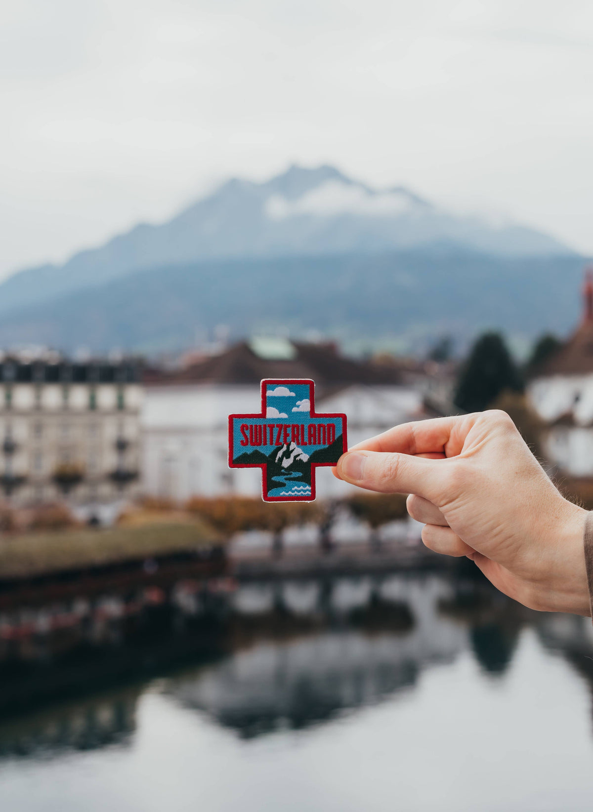 Hand holding a Switzerland sticker with a mountainous landscape in the background