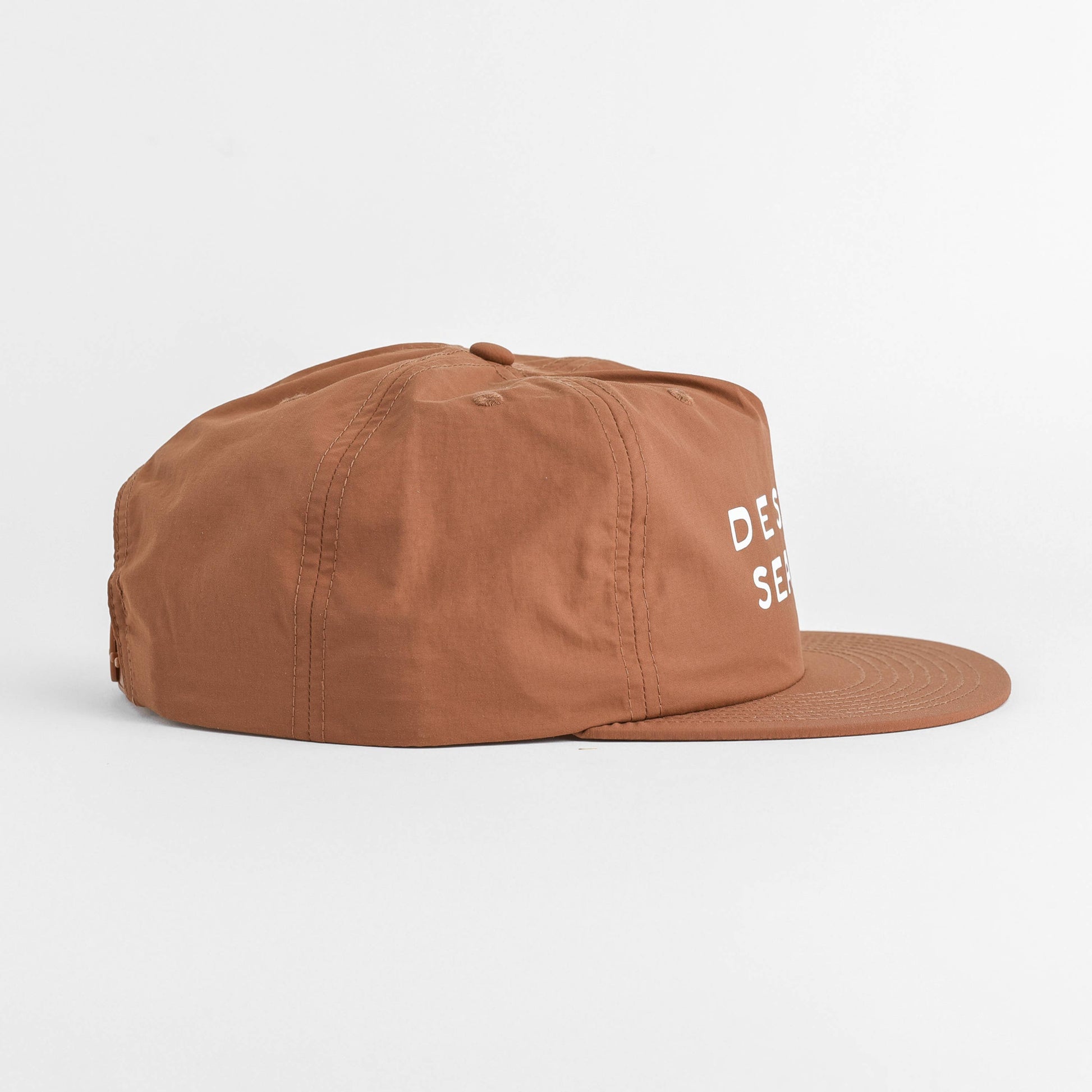 A brown flat-brim cap with white embroidered text on the side, photographed against a clean white background.