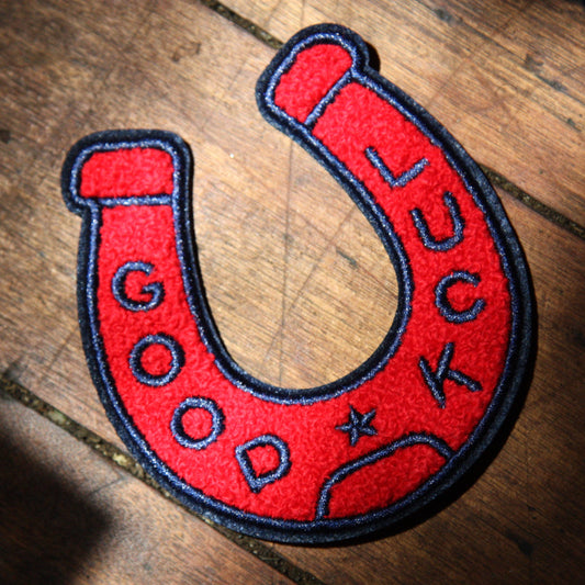 Red horseshoe-shaped patch with 'Good Luck' text on a wooden surface