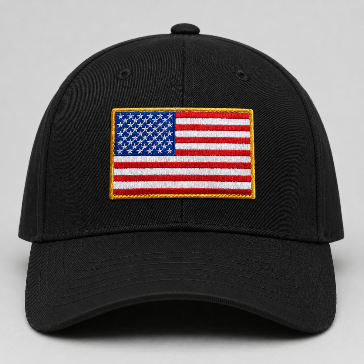 A black baseball cap featuring an embroidered American flag patch on the front, set against a neutral light gray background.
