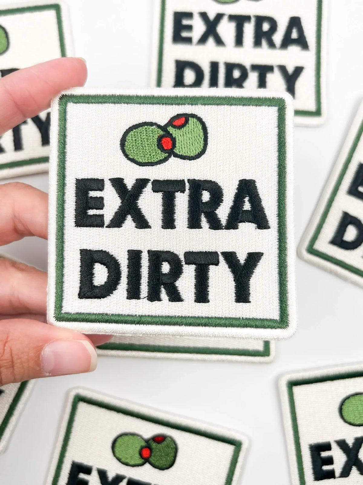 Patch with 'Extra Dirty' text and avocado graphic held by a hand, surrounded by more patches.