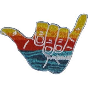 Embroidered patch shaped like a shaka hand sign, featuring a sunset gradient on the fingers and ocean waves in blue on the palm, shown on a plain white background.