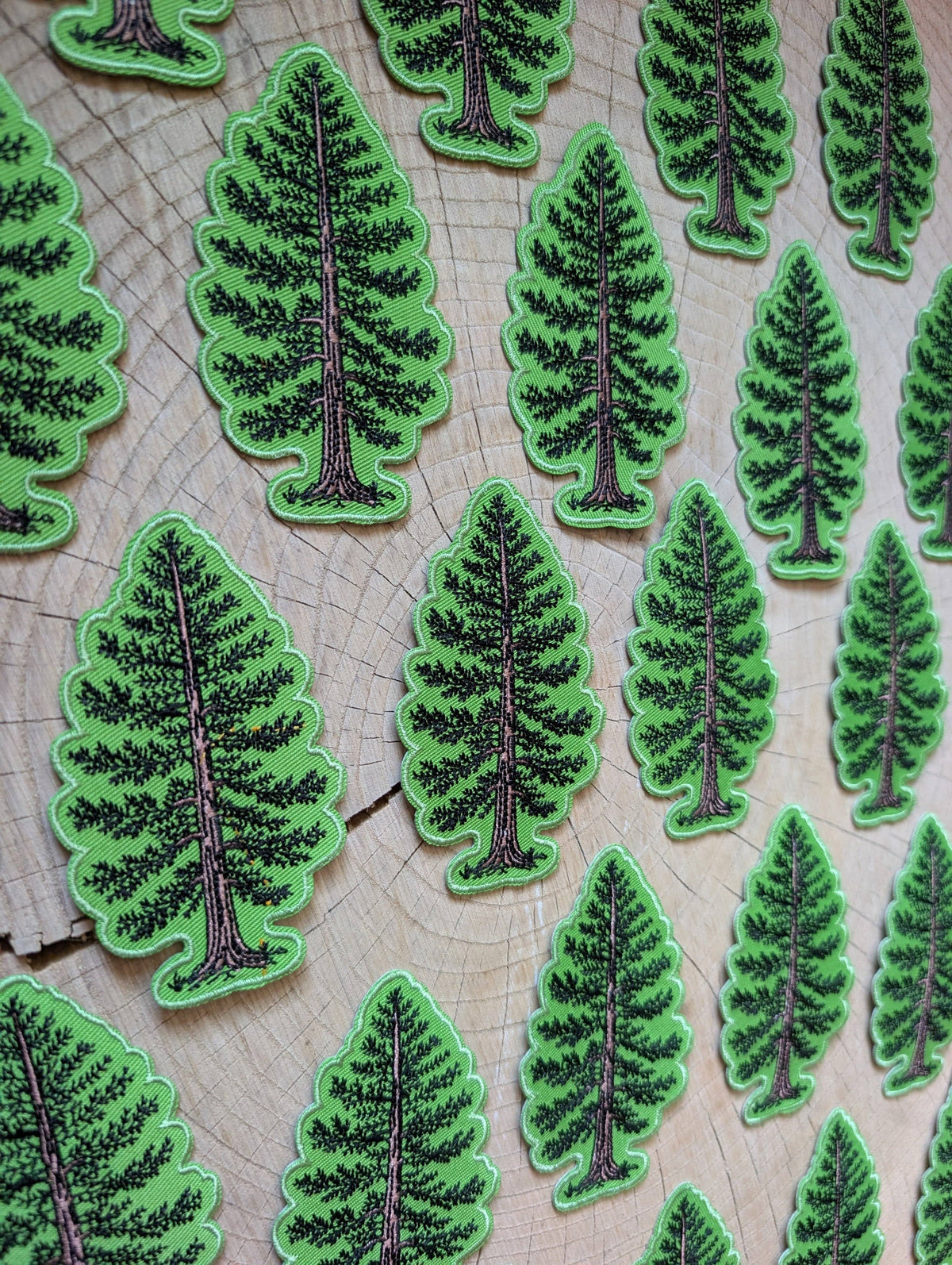 Green pine tree shaped patches with black textured detailing, arranged on a light wood grain background.
