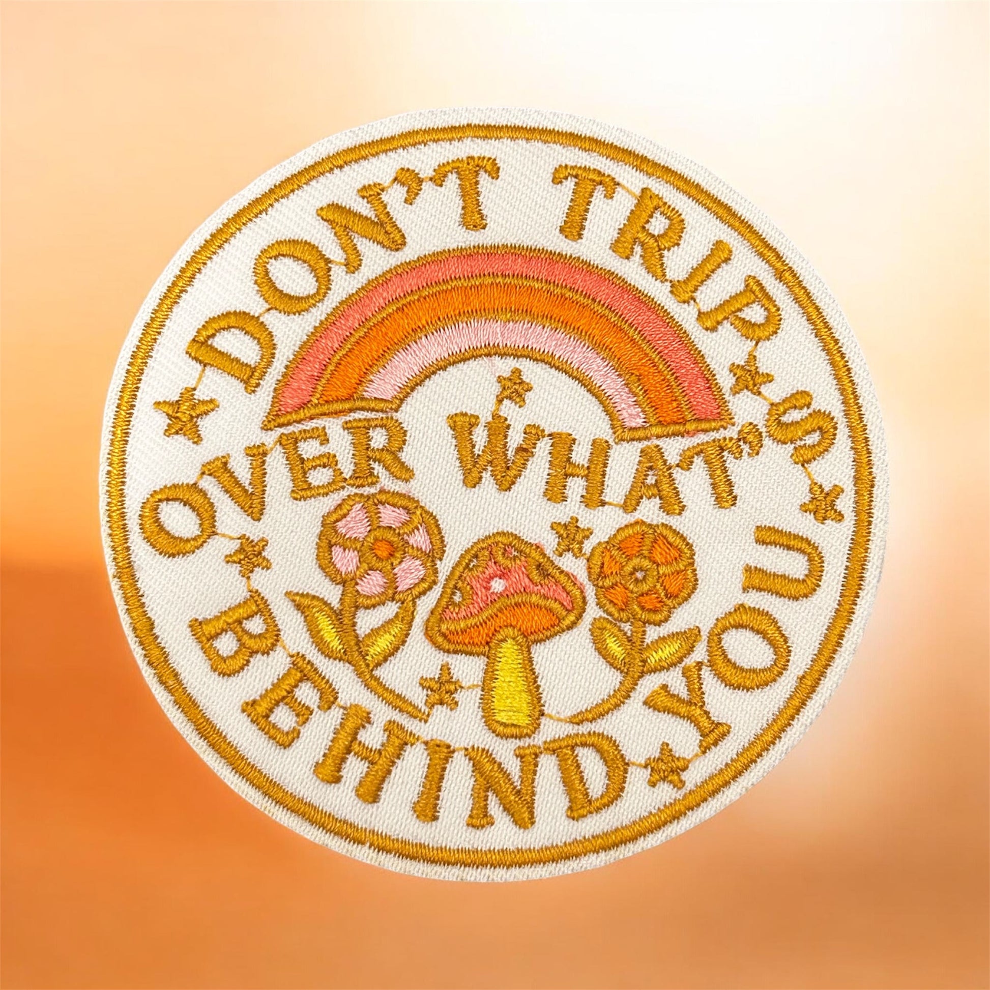 Embroidered patch with text 'Don't trip over what you behind' and a rainbow on a gradient background