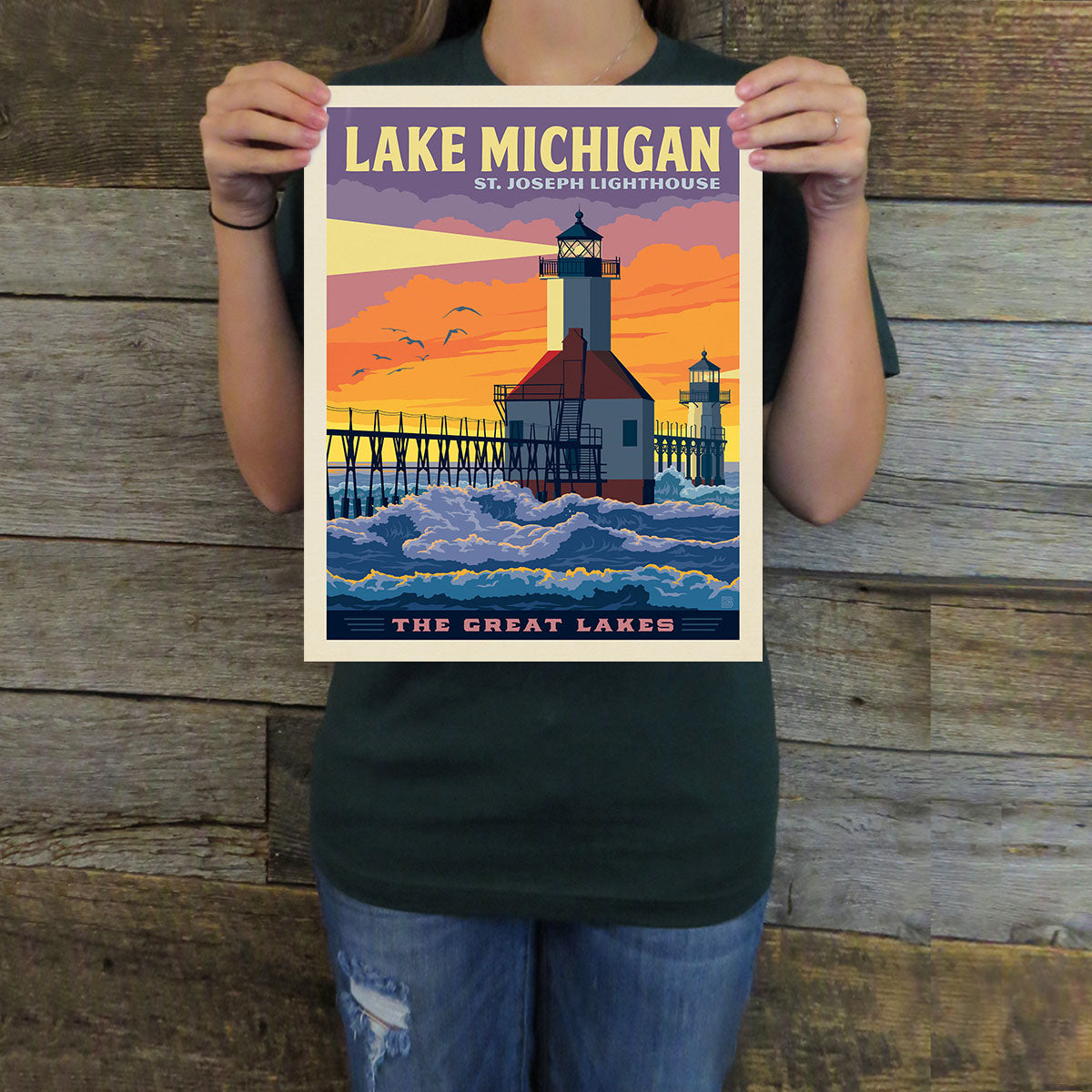 Person holding a poster of Lake Michigan with St. Joseph Lighthouse against a wooden background