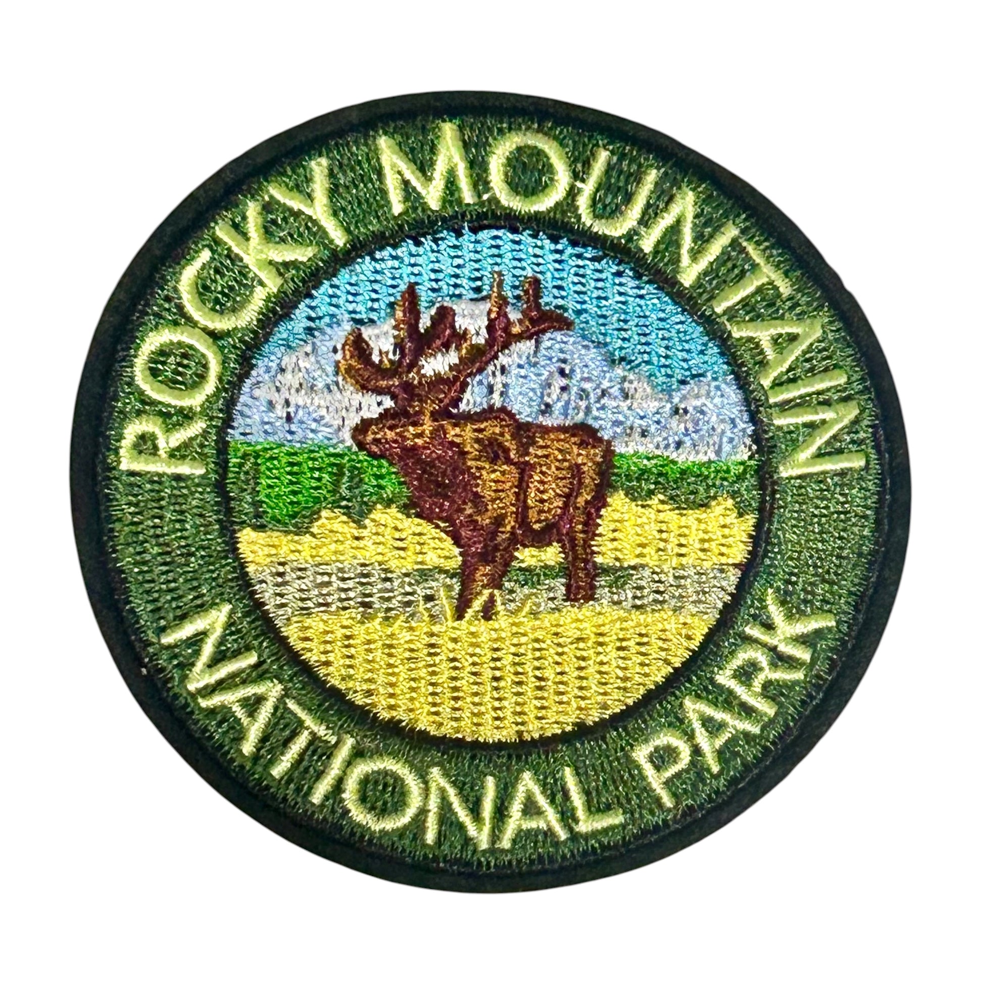 An embroidered circular patch for Rocky Mountain National Park, featuring a brown moose in a yellow field with green hills, a blue sky, and white mountains, surrounded by green border text reading 'ROCKY MOUNTAIN NATIONAL PARK'.