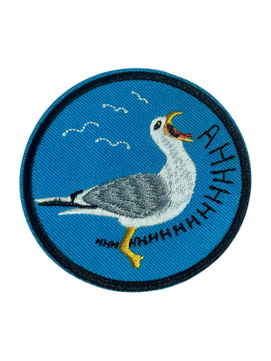 A funny circular embroidered patch featuring a seagull with its beak open, set against a bright blue background with the word 'AHHHH' stitched in black along the right side.