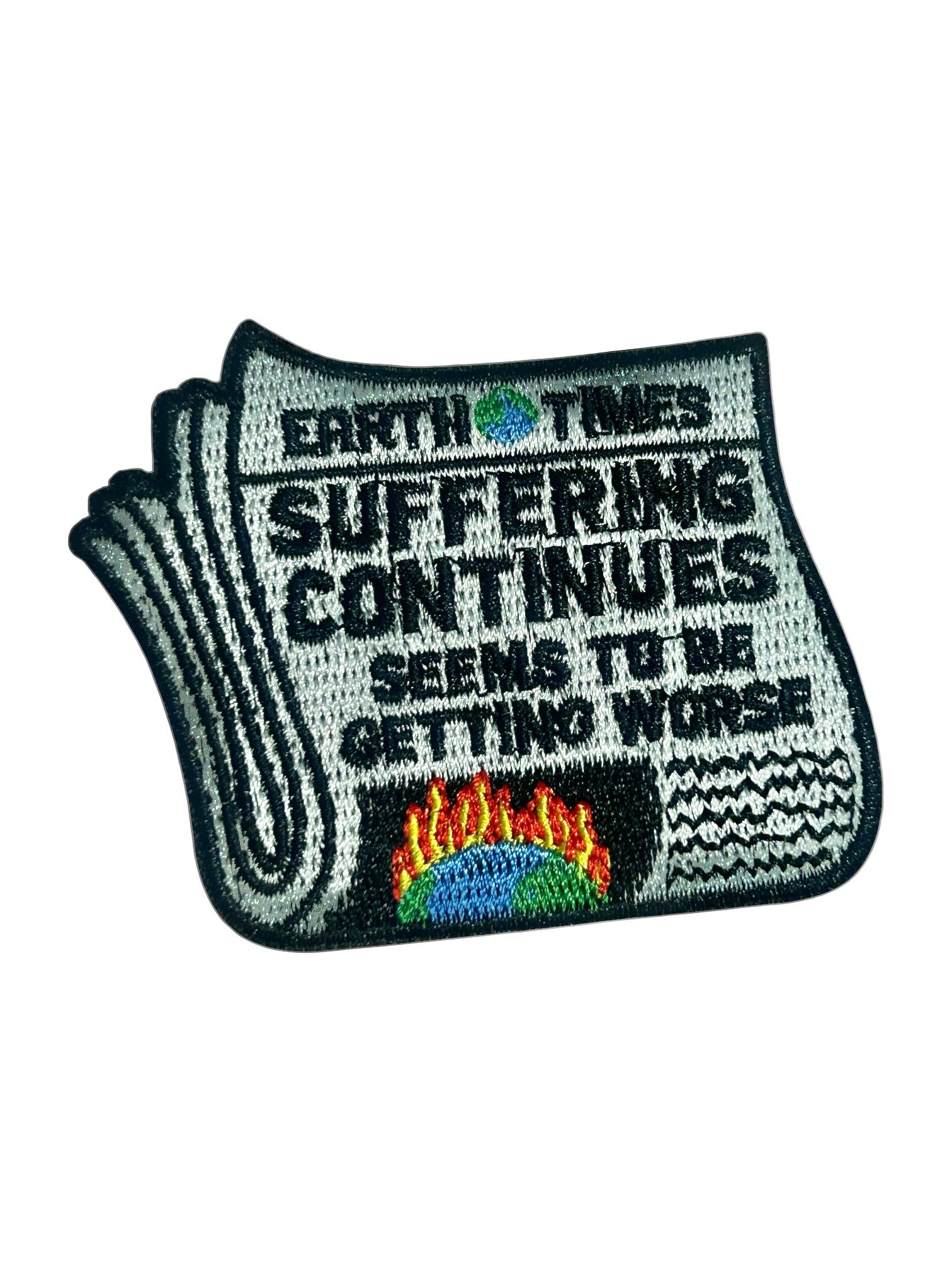 An embroidered patch shaped like a folded newspaper with the text 'EARTH TIMES SUFFERING CONTINUES SEEMS TO BE GETTING WORSE' and a small multicolor globe-and-flames graphic near the bottom, shown on a plain white background.