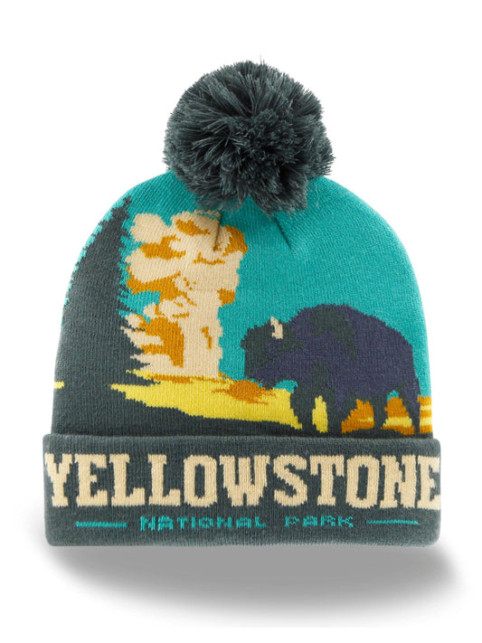 A Yellowstone National Park knit beanie hat featuring a dark teal and gray design with a bison, tree, and sunset motif, topped with a dark gray pom-pom. The folded cuff reads 'YELLOWSTONE NATIONAL PARK' in cream and teal.