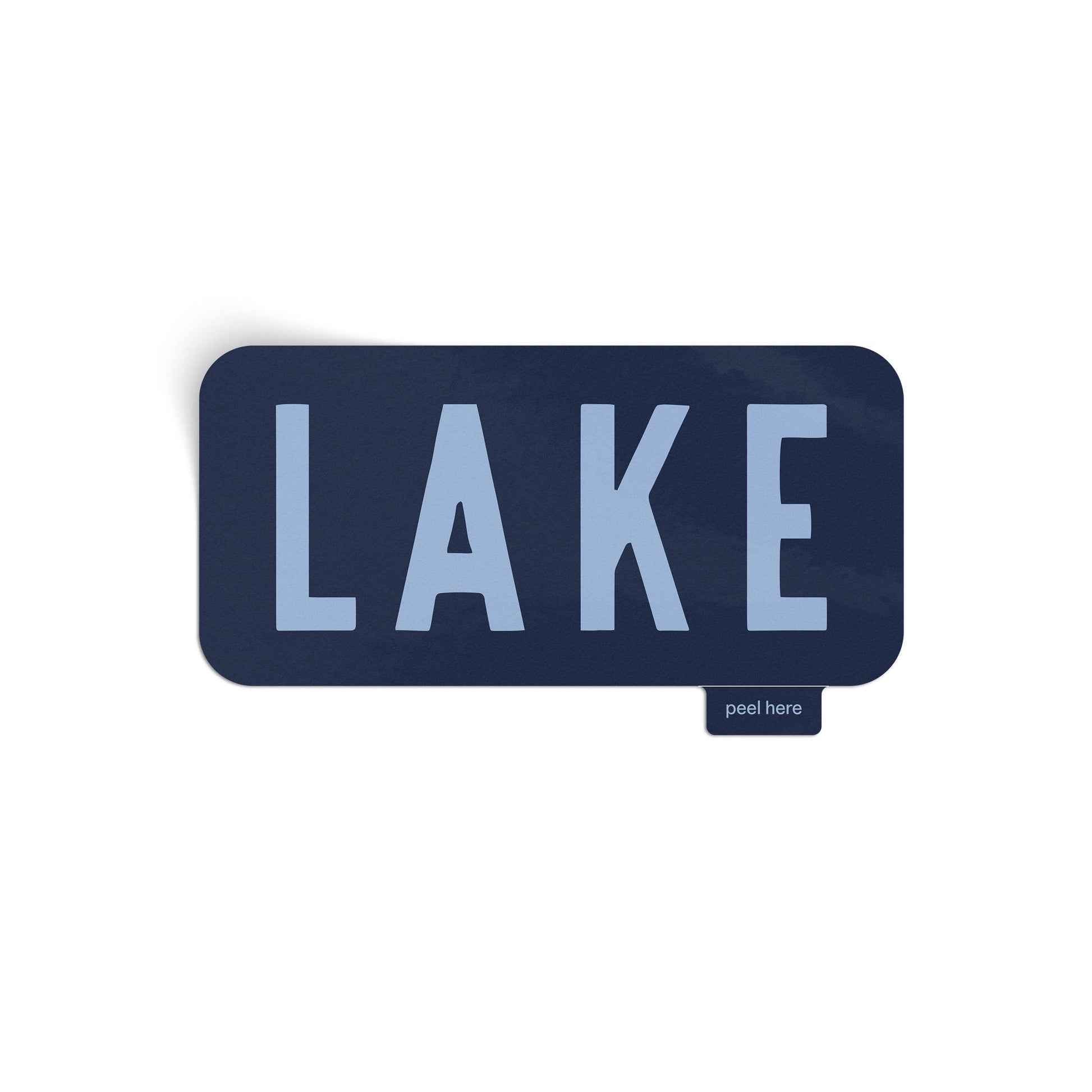 A rectangular dark navy blue peel-and-stick decal with rounded corners, featuring the word 'LAKE' in light blue-gray capital letters. A small tag on the bottom right reads 'peel here'.