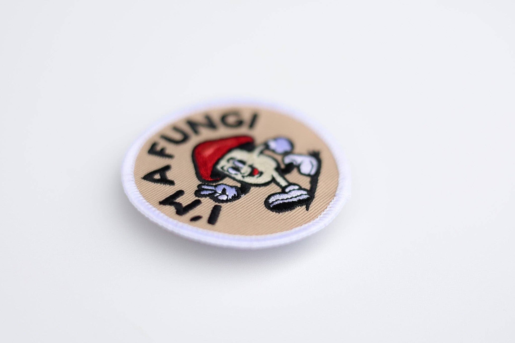 A circular embroidered patch with a white border on a light gray background. The patch has a beige center with the text 'A FUNGI N.