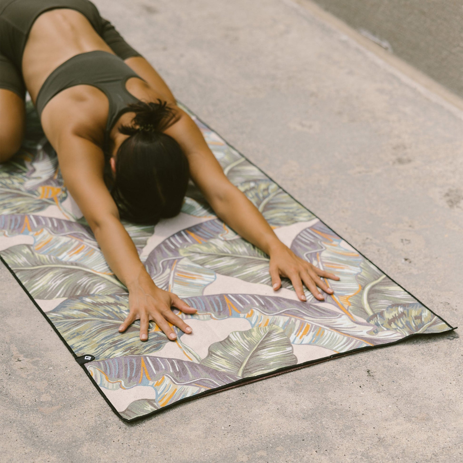 Person stretching on a colorful yoga mat with leaf patterns outdoors.