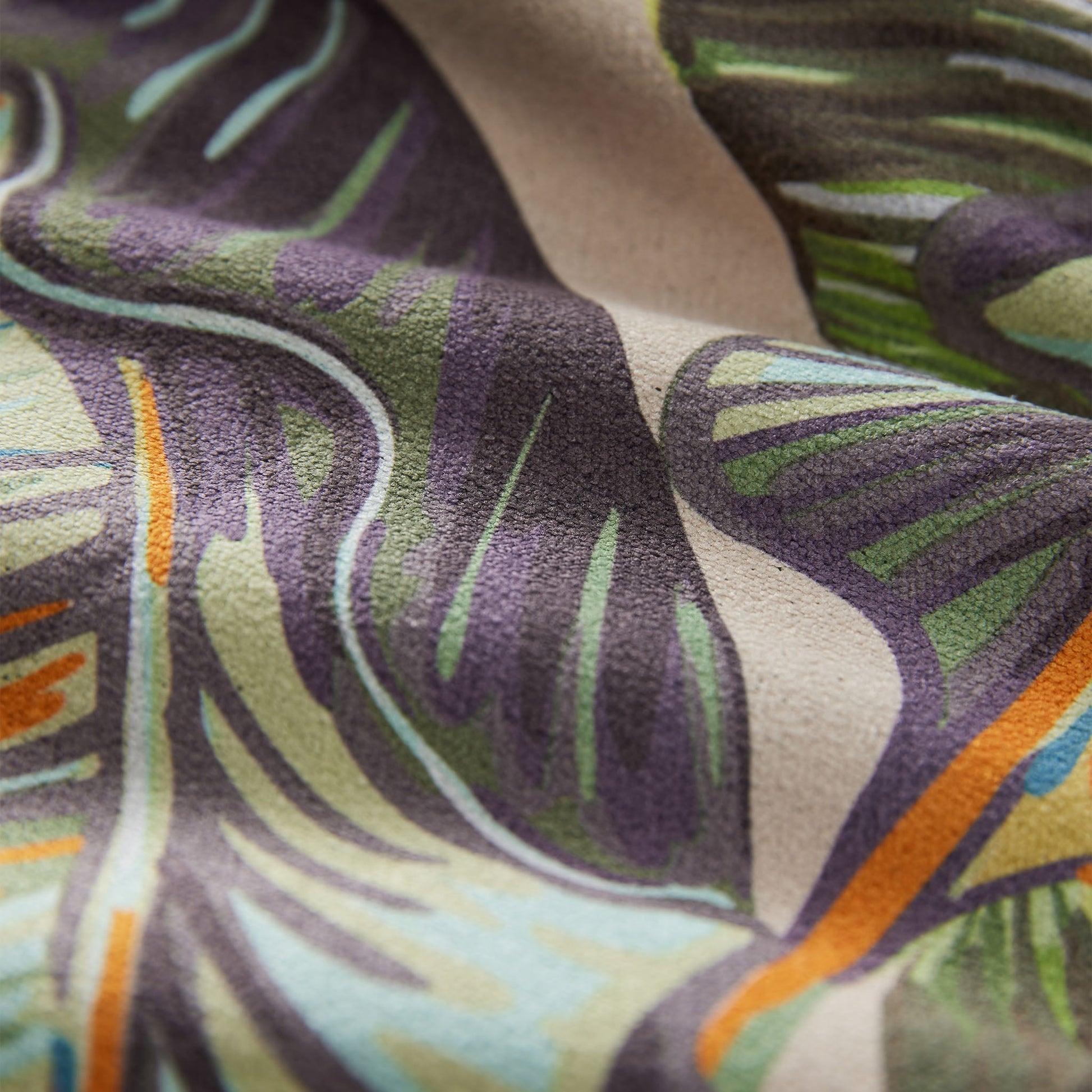 Close-up of a fabric with a leaf pattern in green, purple, and orange.