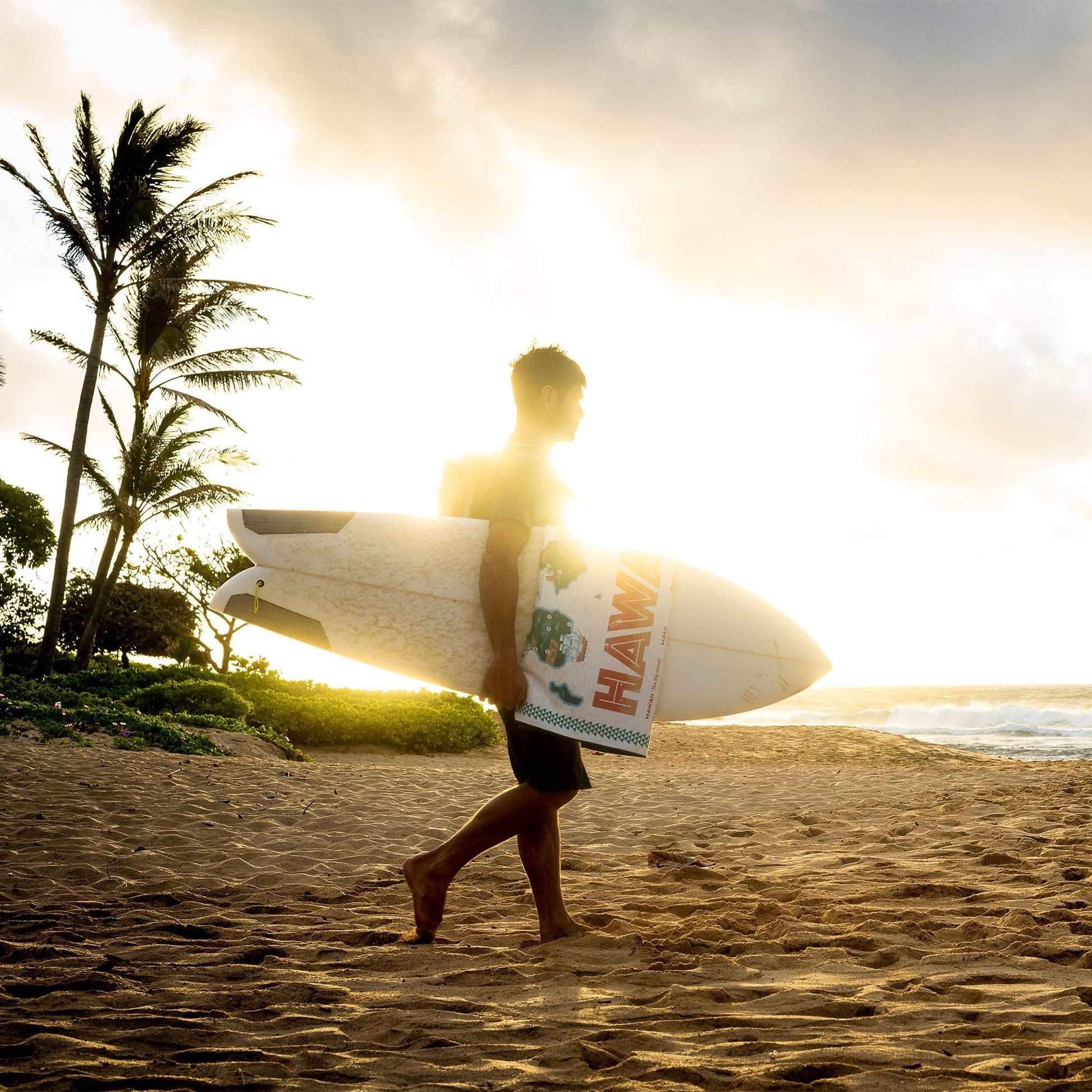 Person walking on a beach with a surfboard at sunset