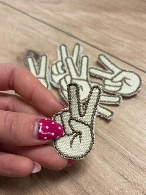 Hand holding a peace sign patch with more patches on a wooden surface